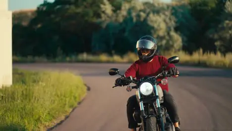 A man in a red sweater and a motorcycle helmet effectively turns on the road on a motorcycle in sunny weather Motorcycle riding as a hobby