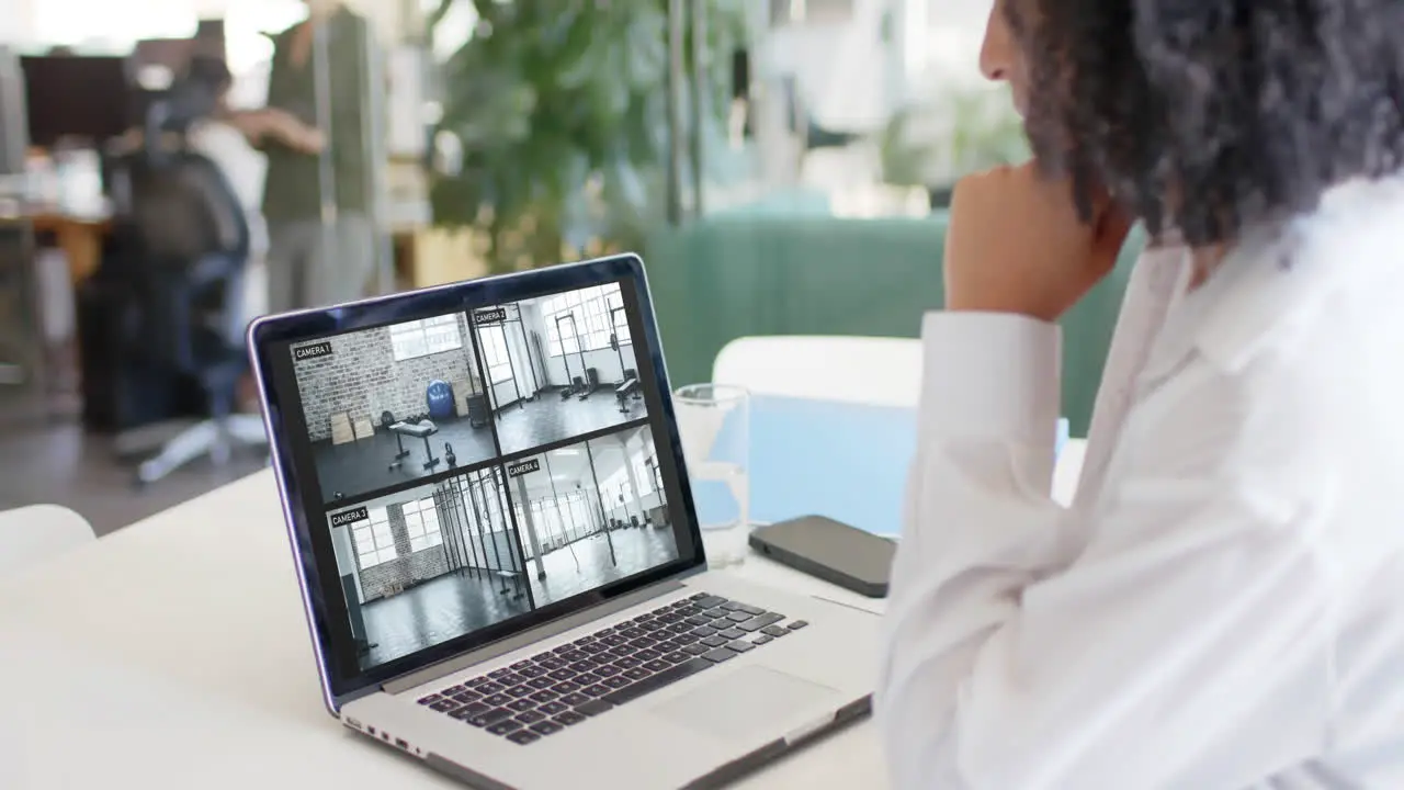 Biracial female security officer watching cctv camera views on laptop in office slow motion