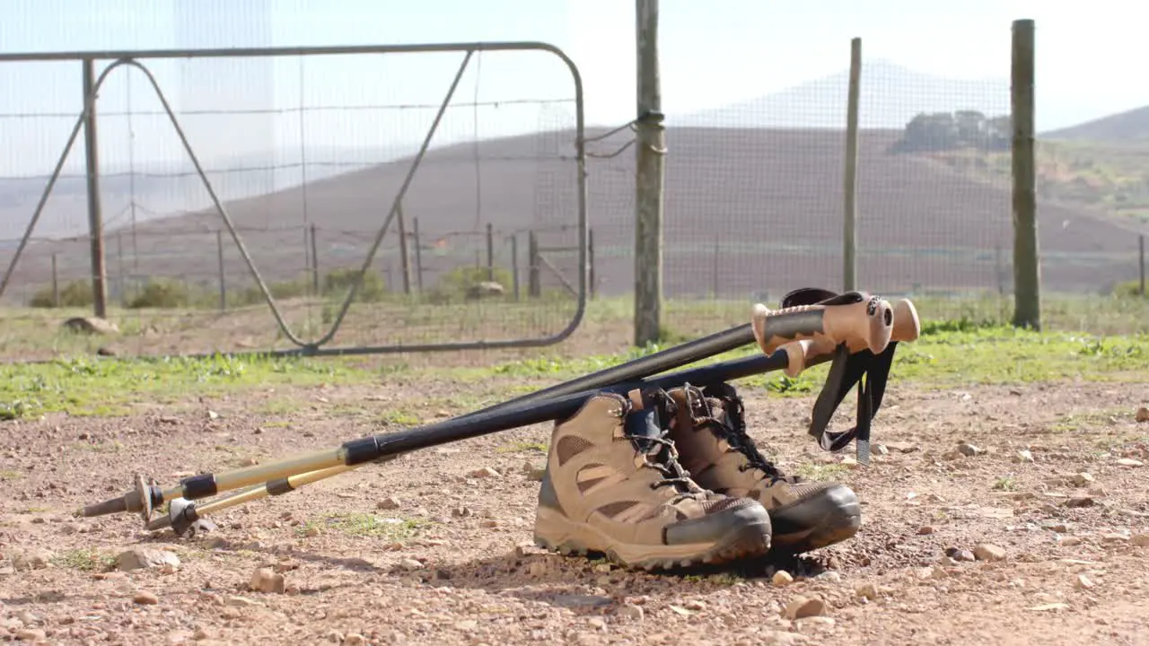 Hiking shoes and sticks on ground over fence and countryside slow motion