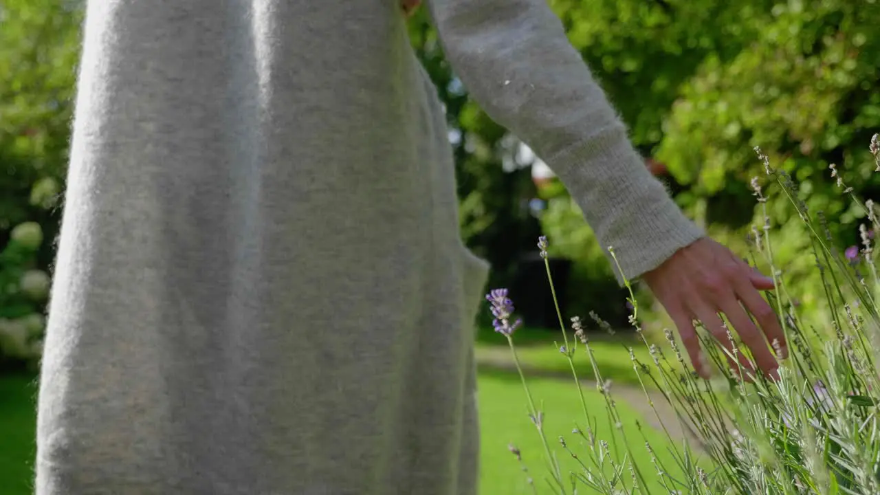 Slow motion close up shot following a young woman walking through a lush green garden moving her hand through the plants vegetation high grass