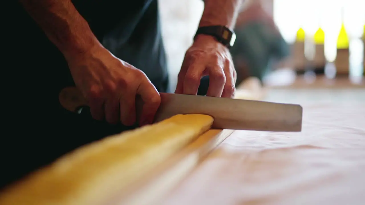 Slowmotion panning shot of an Italian chef cutting handmade pasta over a raw wood chopping table