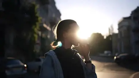 A girl in stylish glasses eats ice cream in a waffle cone in the rays of sunset Casual clothes Walking in the city Side view