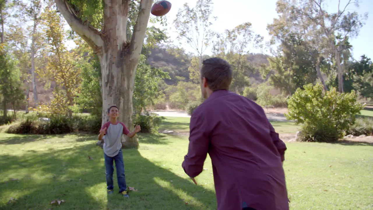 Boy and his dad playing with American football in a park