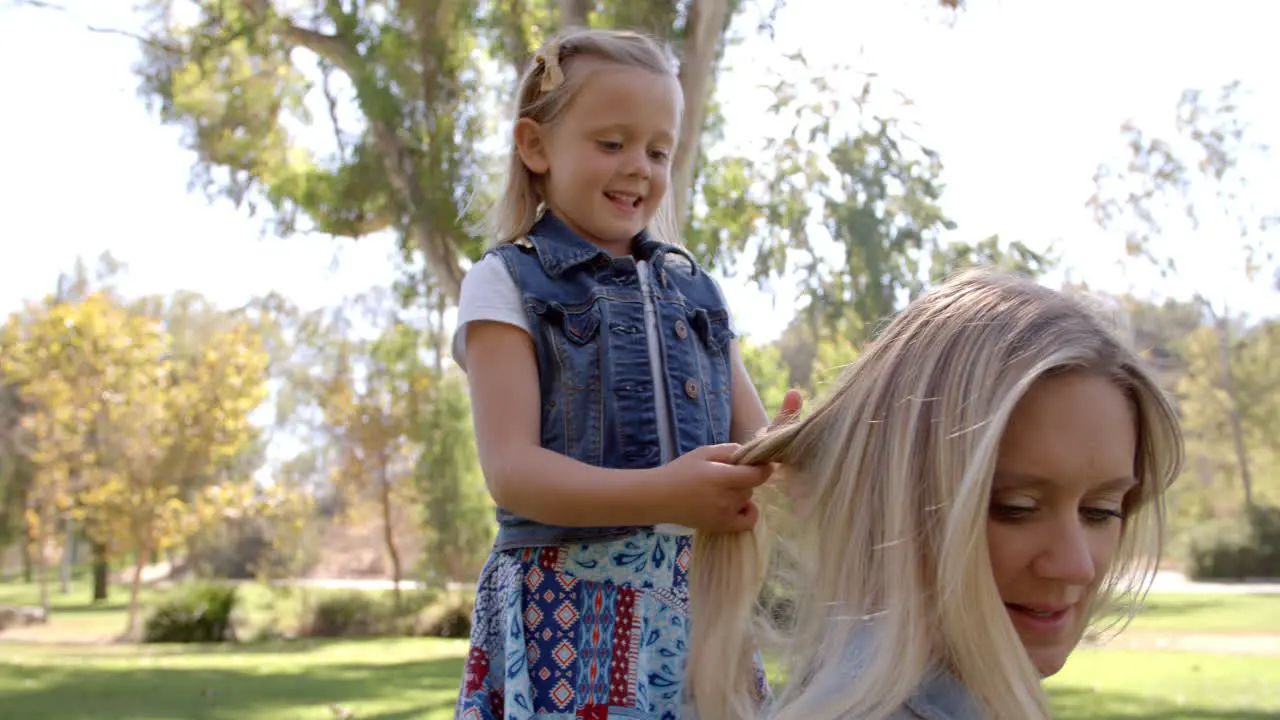 Young daughter braiding mother's hair in a park front view