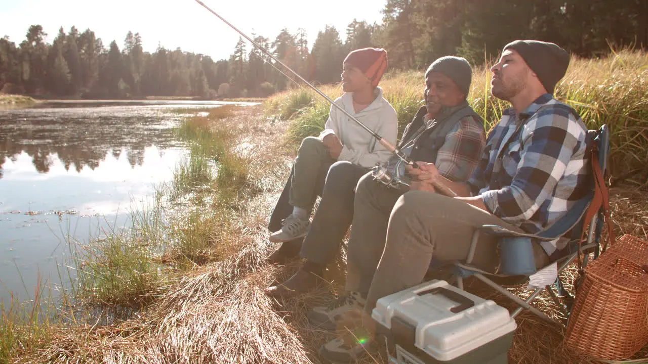 Grandfather father and son sit fishing by a rural lake