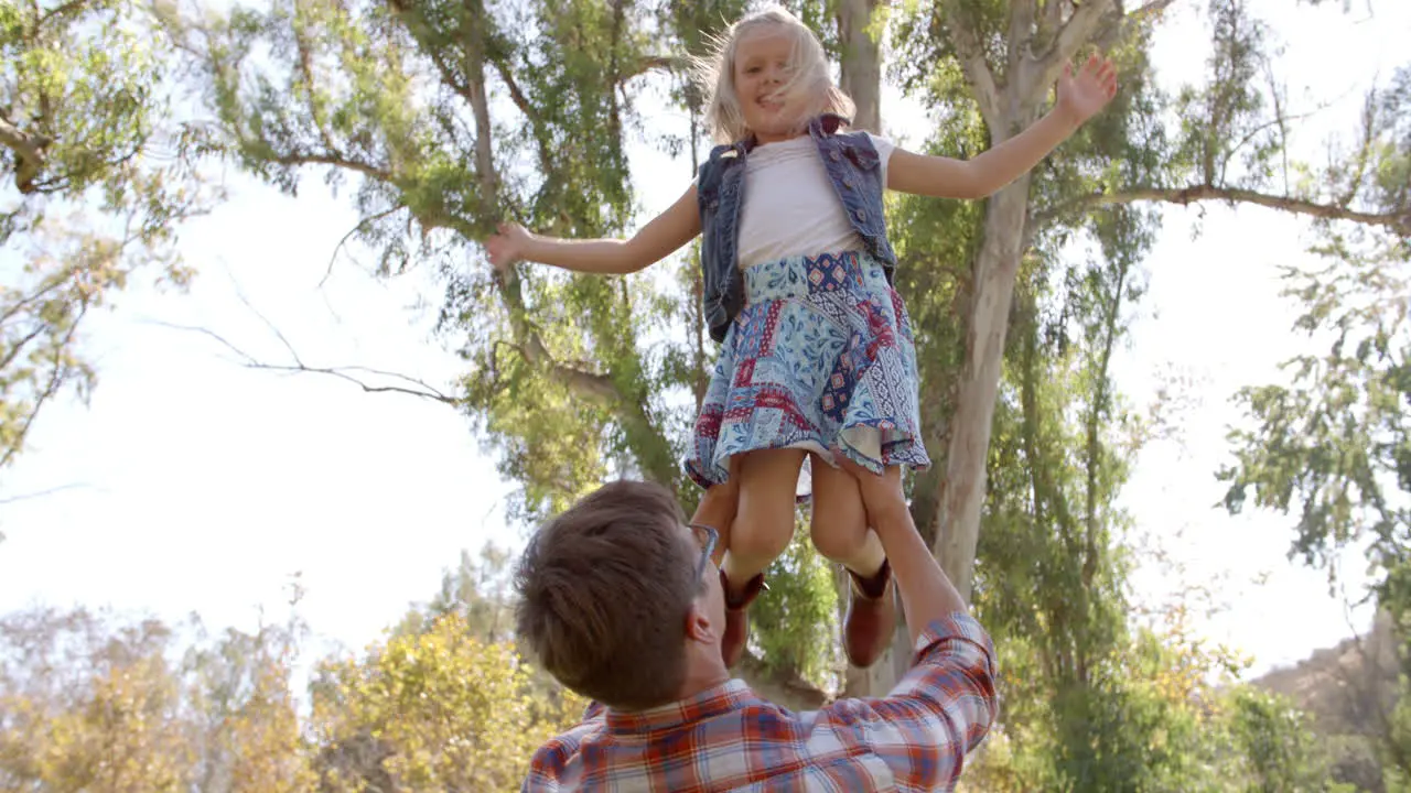 Dad holding his young daughter in the air in a park