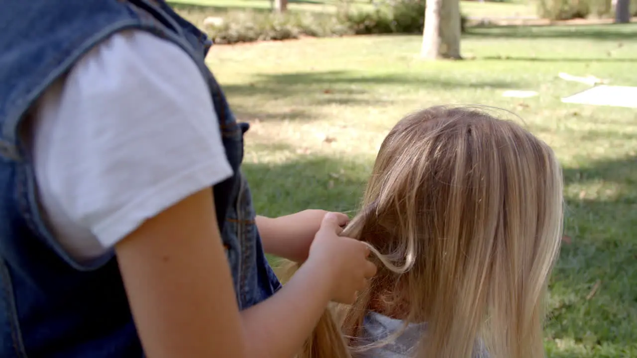 Young daughter braiding mother's hair in a park