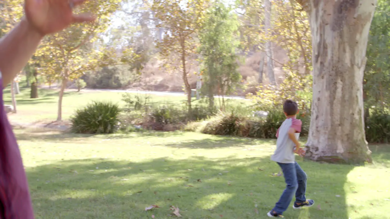 Dad and son passing American football to each other in park