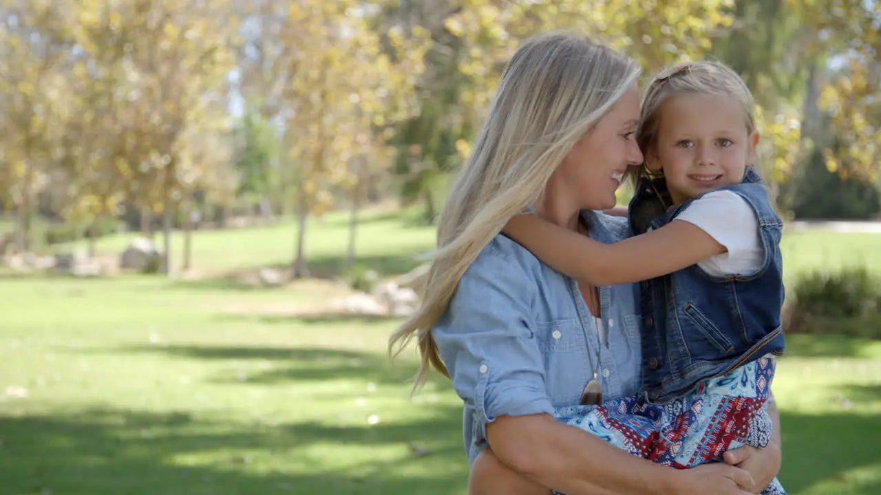 Mother carrying young daughter in park walks in to focus