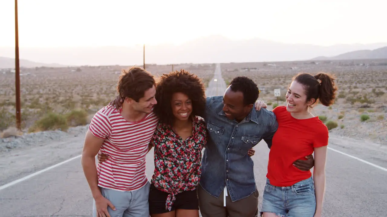 Four happy friends standing on a desert highway close up