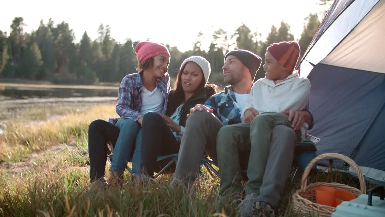 Parents and two children relaxing outside tent on camping trip