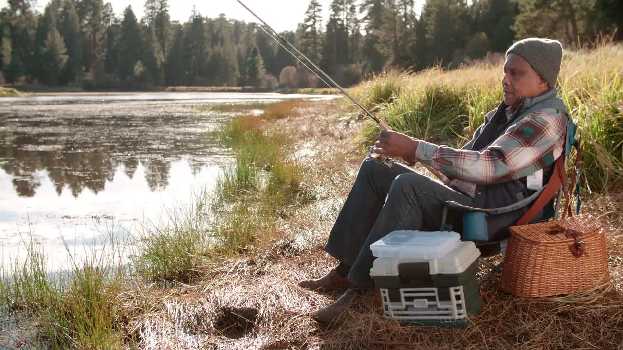 Senior black man on a camping trip fishing by a rural lake