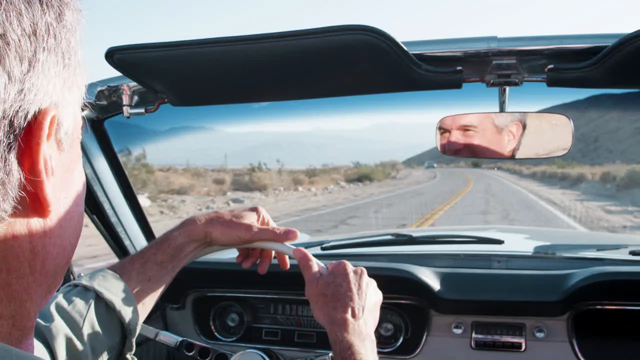 Senior man driving old convertible over shoulder close up