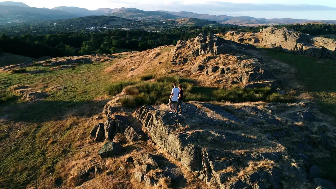 Drone shot circling adult couple standing on a rocky peak overlooking Lake Windermere Lake District UK