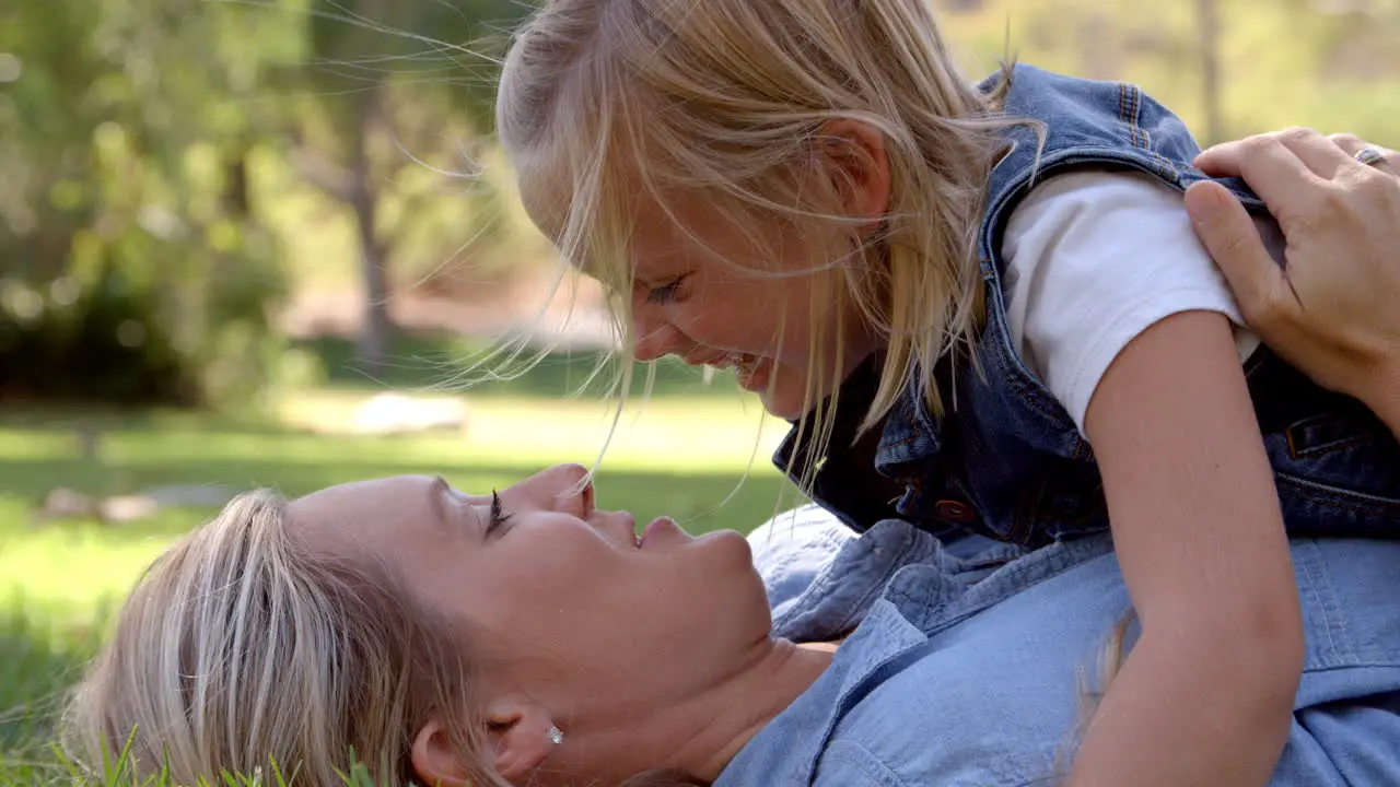 Young daughter lying on her mother in a park close up