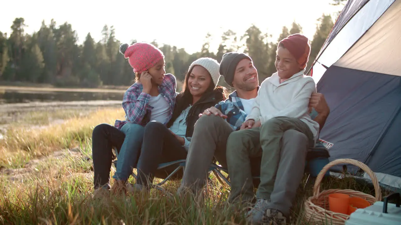 Parents and two children sit talking outside tent