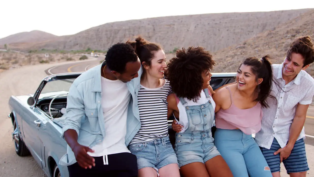 Friends on a road trip take a roadside break sitting on car