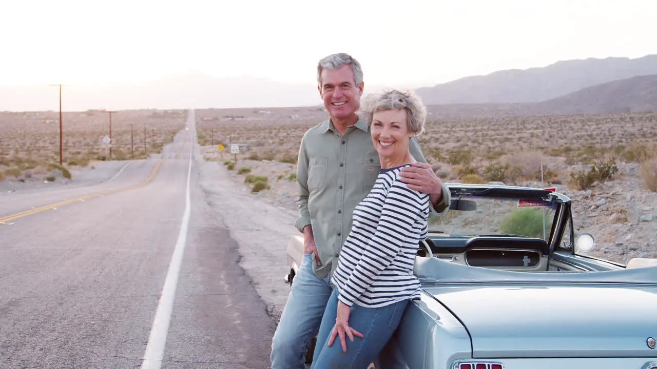 Senior couple on road trip standing by car smiling to camera