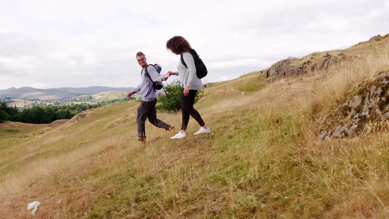 A smiling young adult couple walking down a hill holding hands during a mountain hike