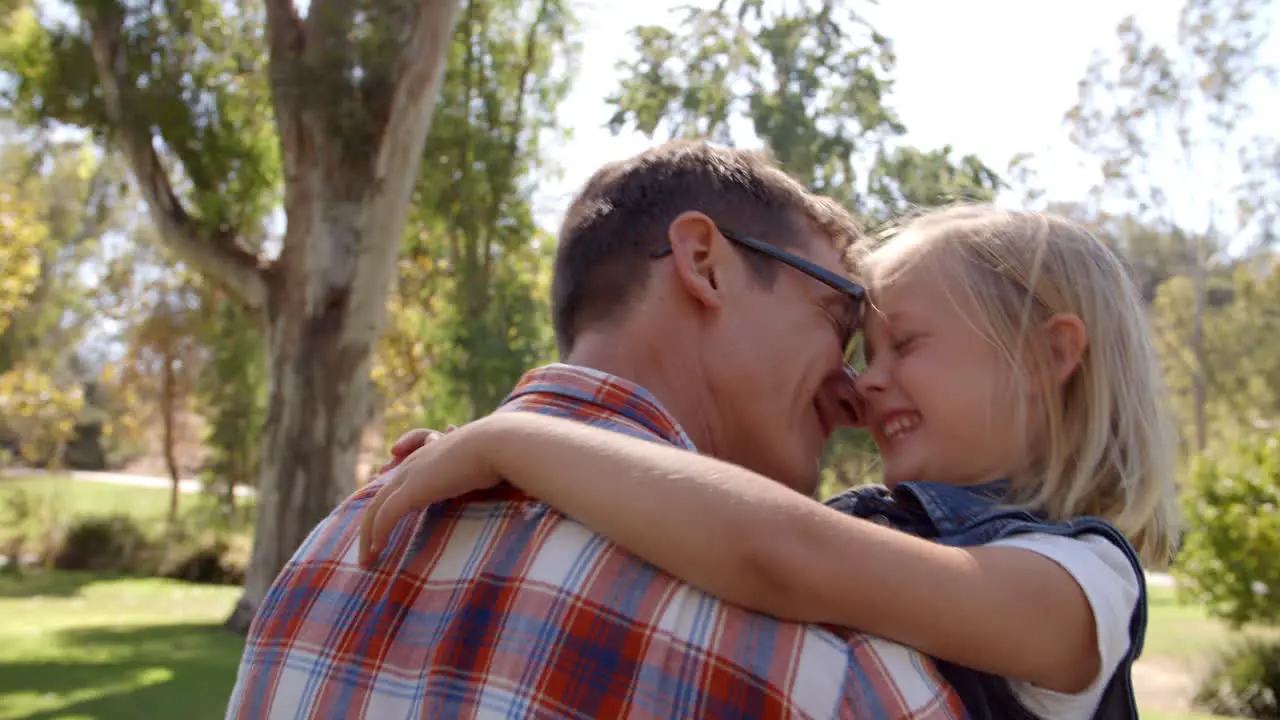 Dad and young daughter pulling faces at each other in a park