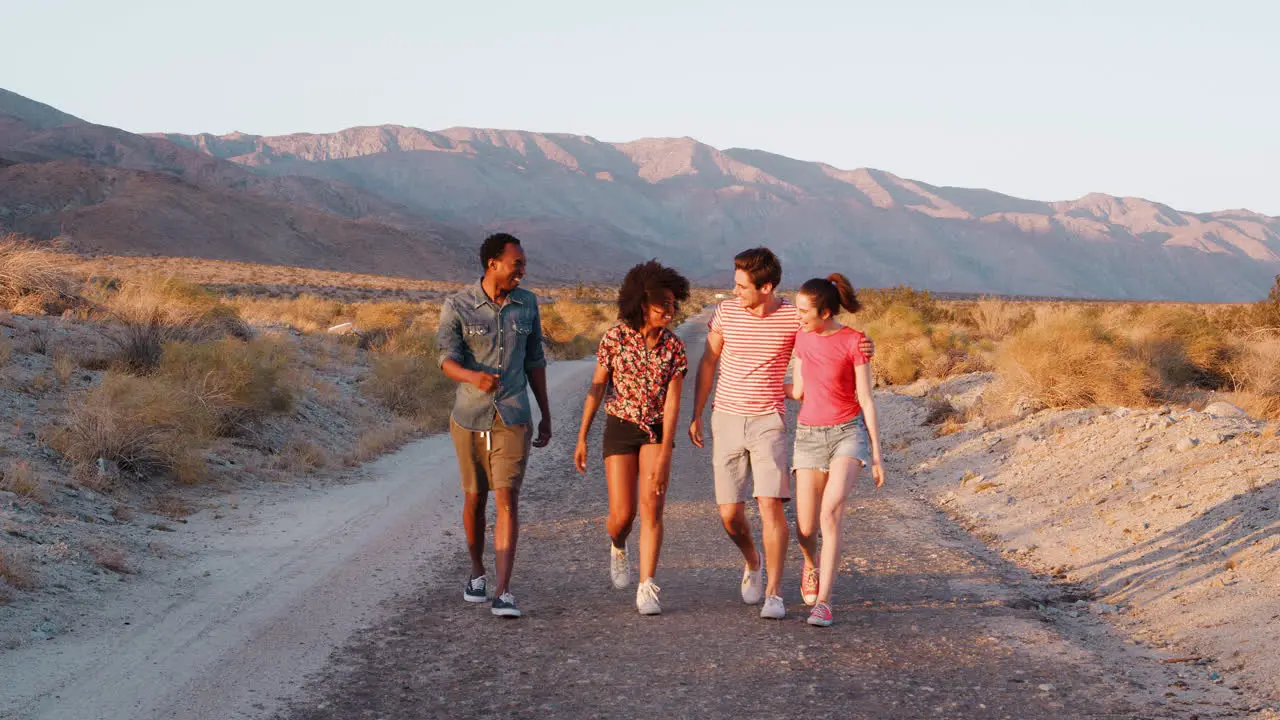 Two young adult couples walking and talking on a desert road