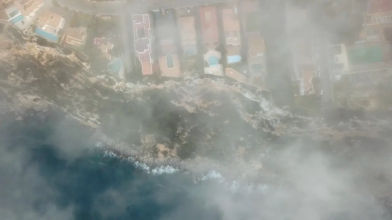 Beautiful top down aerial shot of a coastline with fog clouds everywhere 4k