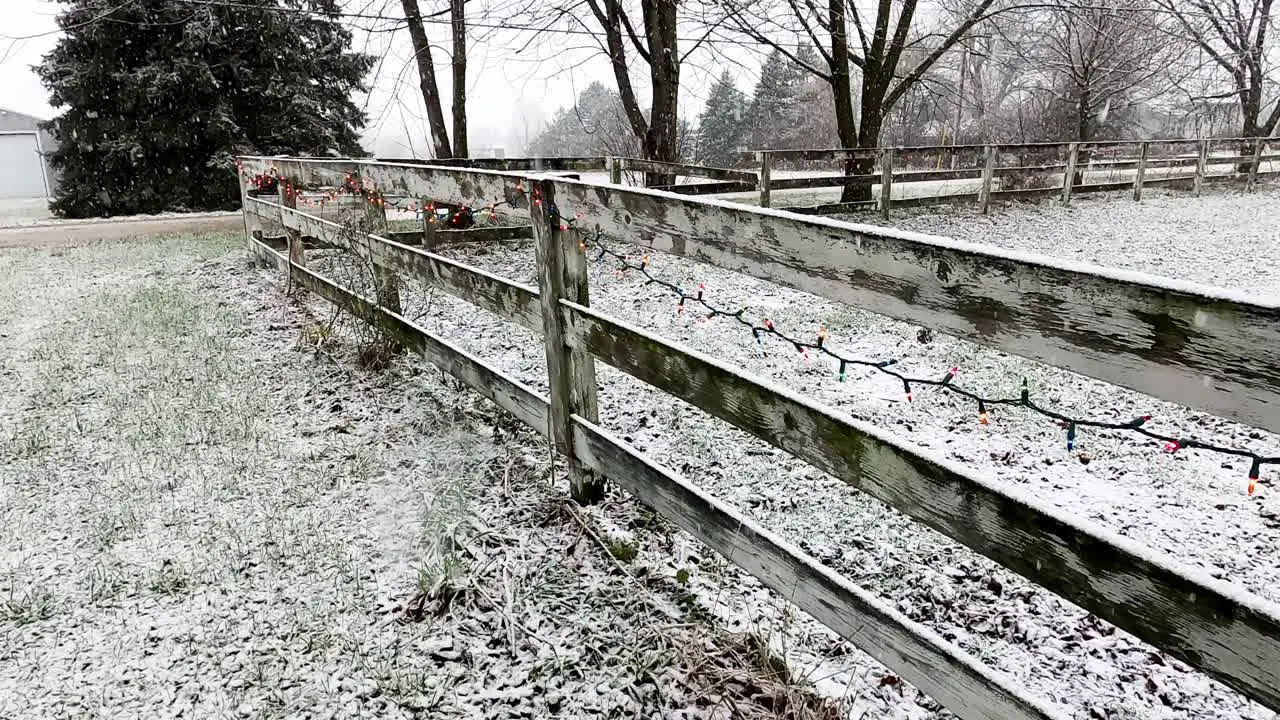 Wooden farm fence decorated with Christmas lights during heavy snowfall