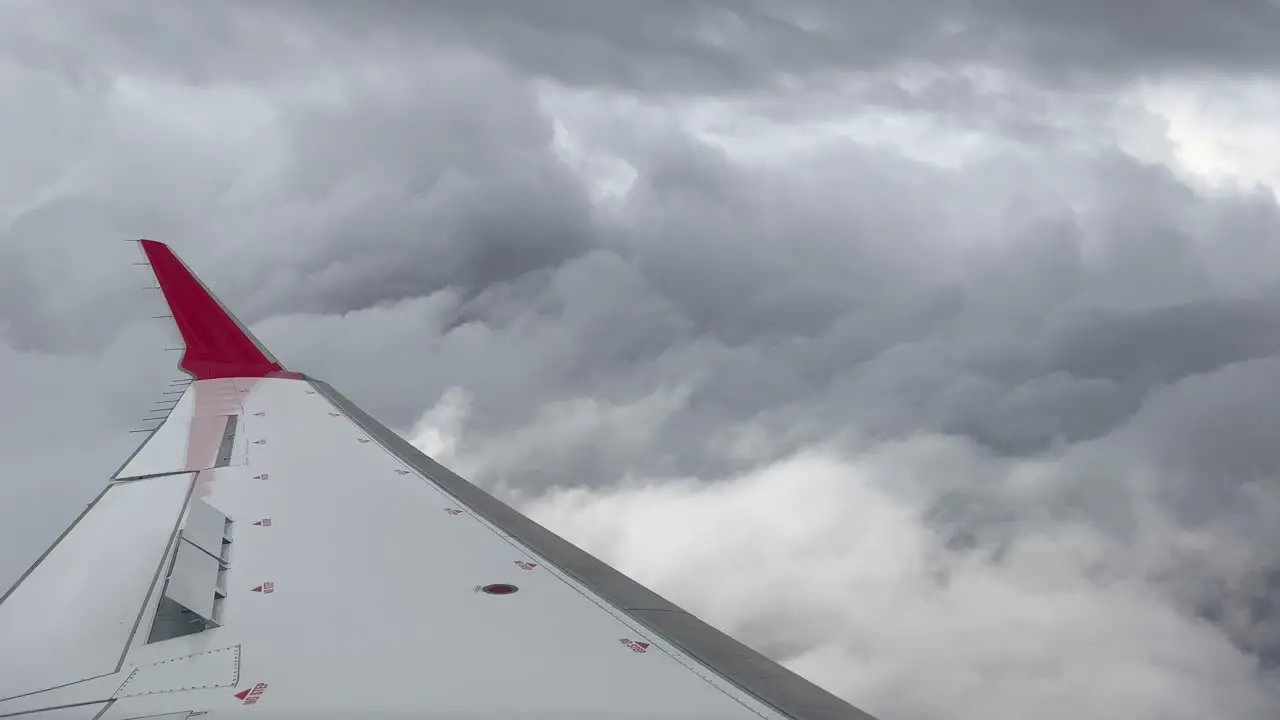 Side view of a medium jet plane crossing a turbulent sky plenty of stormy clouds with the airbrakes deployed and a red winlet