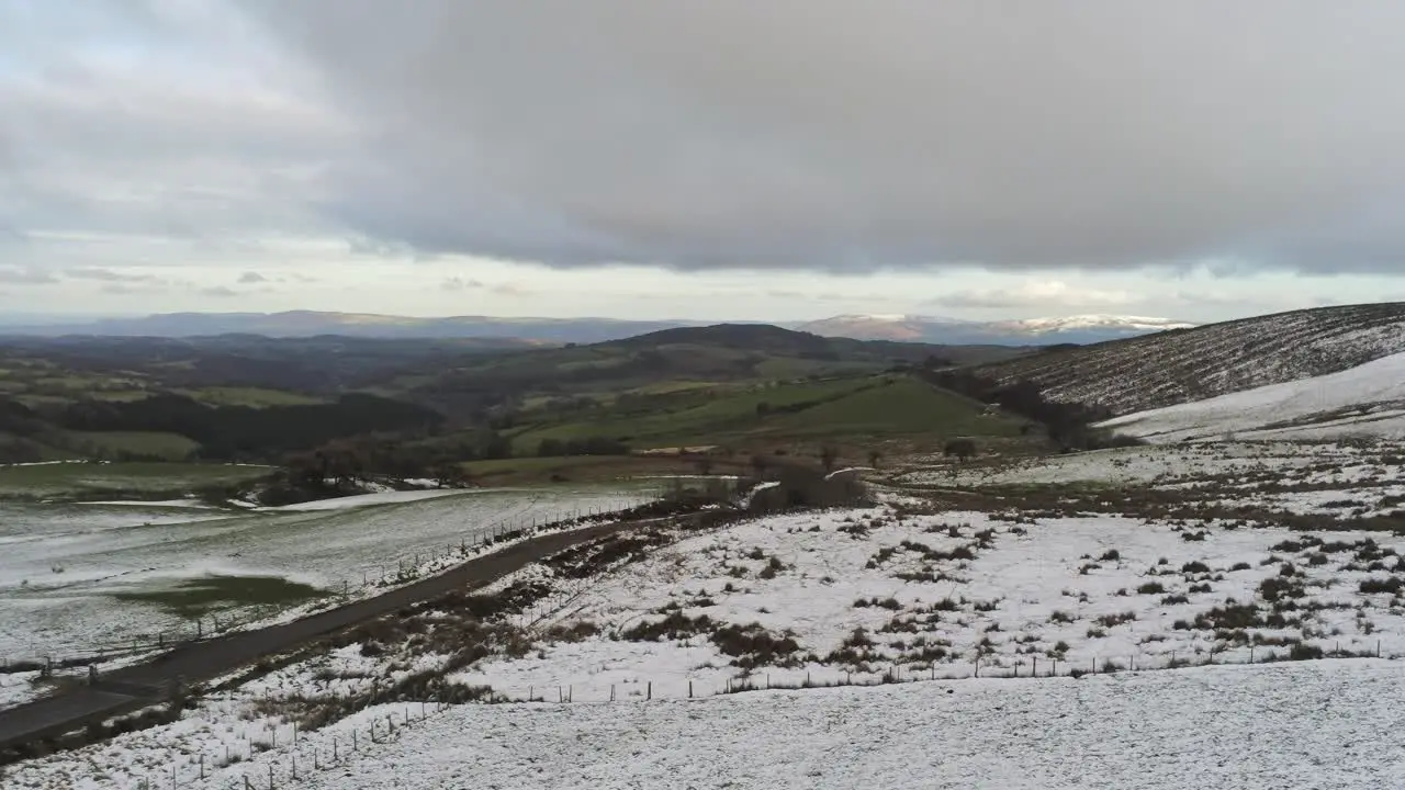 Snowy rural seasonal winter valley countryside aerial agricultural farmland landscape pan right