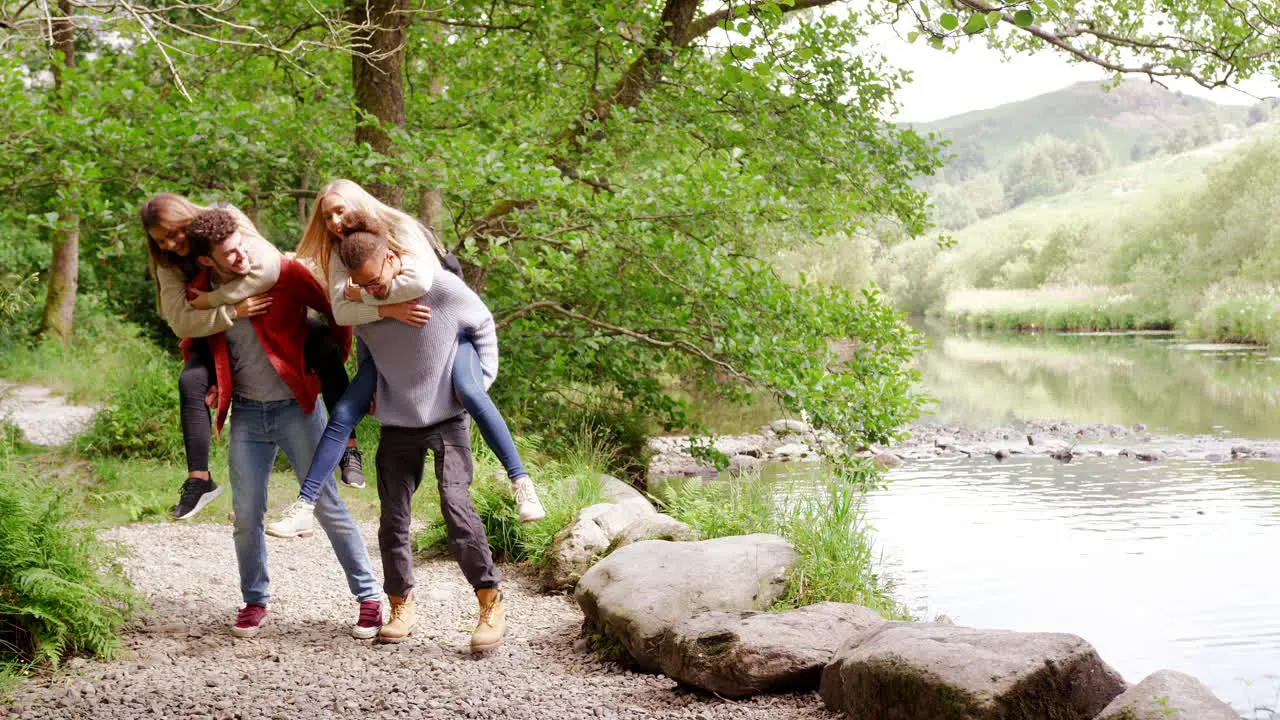 Four young adult friends during a hike men piggybacking their girlfriends handheld