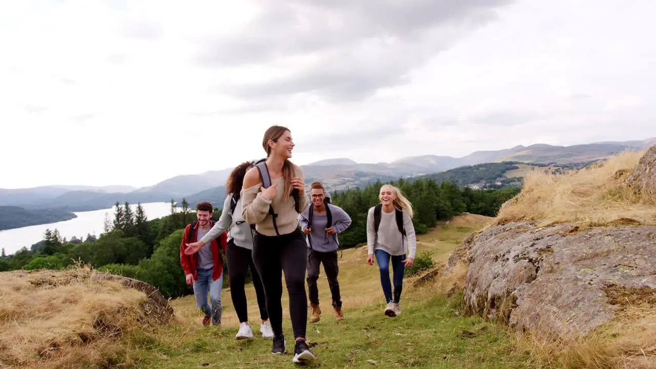 A multi ethnic group of five young adult friends smile while hiking across a field to the summit during a mountain hike close up