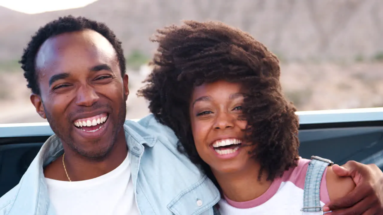 Laughing young couple on road trip sitting on car close up