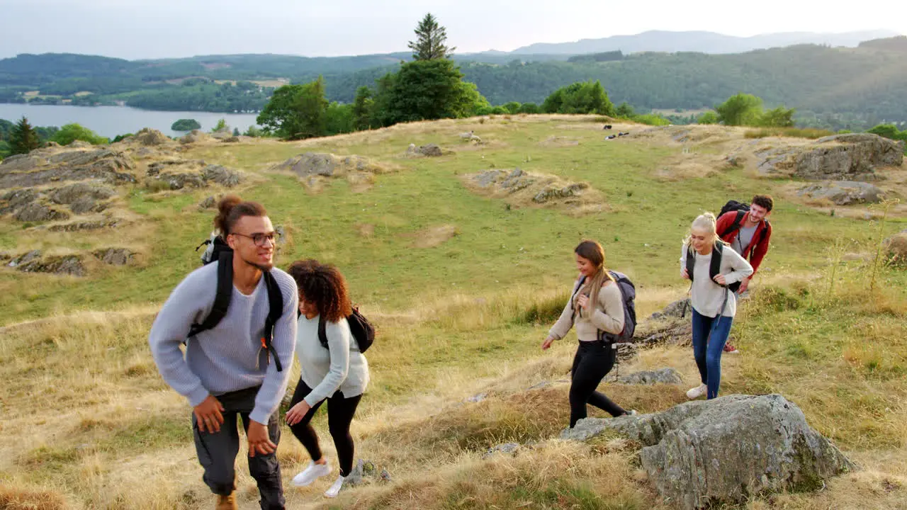 A multi ethnic group of five happy young adult friends hiking across a field to the summit during a mountain hike close up