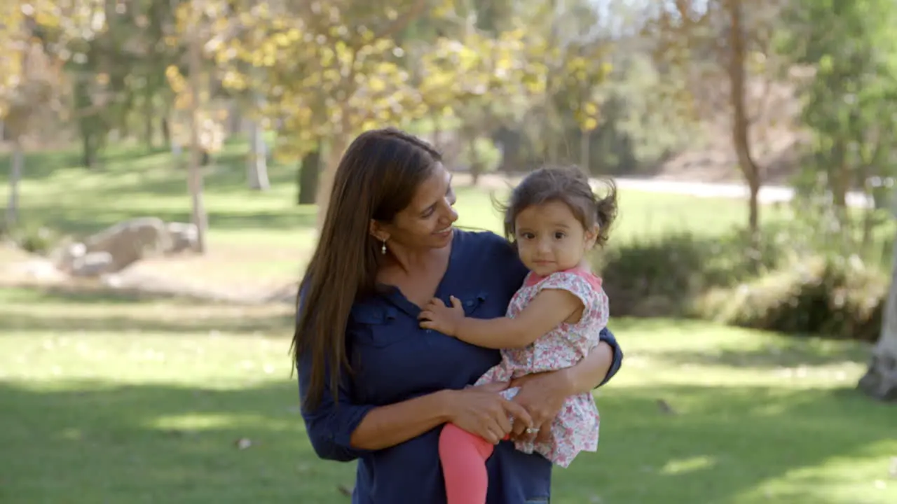 Mixed race Asian mum with toddler in park walks in to focus