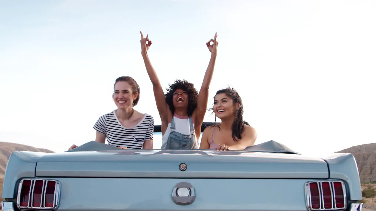 Three female friends in the back of an open top classic car