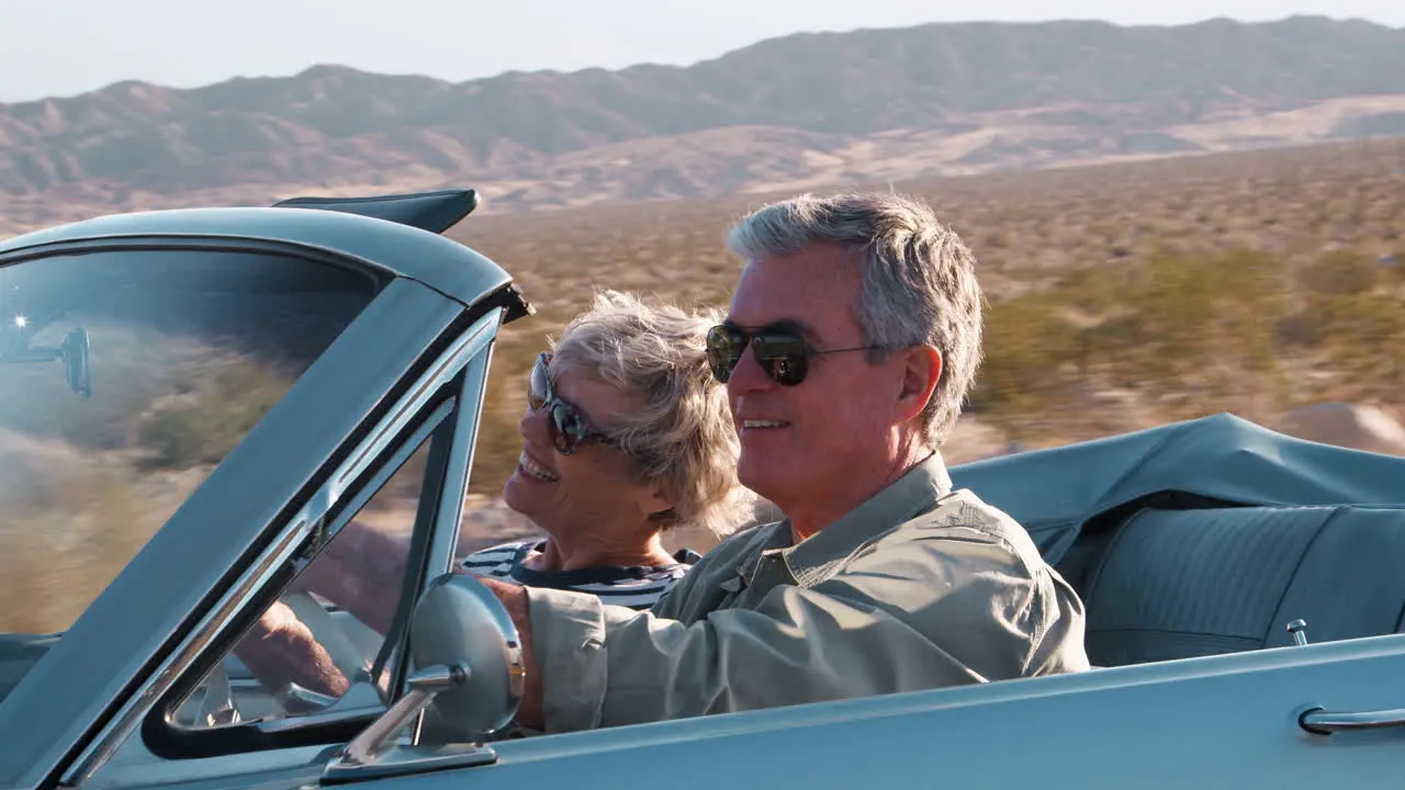 Senior couple driving in open top car on a desert highway