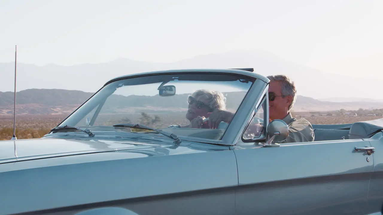 Smiling senior couple driving classic convertible on highway