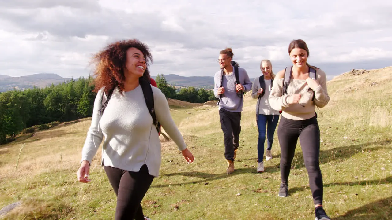 A multi ethnic group of five happy young adult friends walking across a field during a mountain hike close up