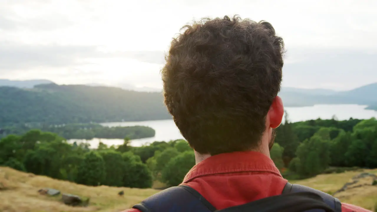 A young adult Caucasian man standing at the summit admiring the view during a mountain hike close up back view