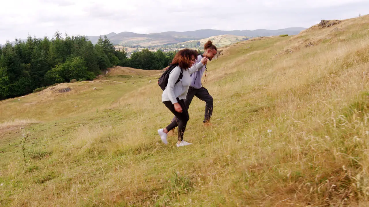 A smiling young adult couple holding hands while hiking to the summit across a field during a mountain hike