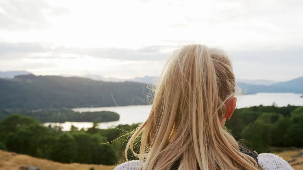 A young blonde woman standing at the summit the view during a mountain hike close up back view