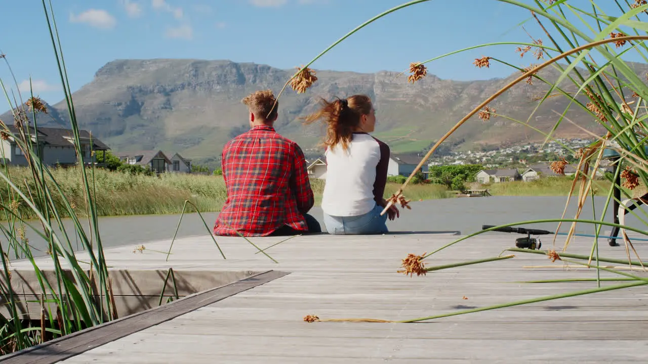 Couple sitting on a jetty by a lake and mountains back view