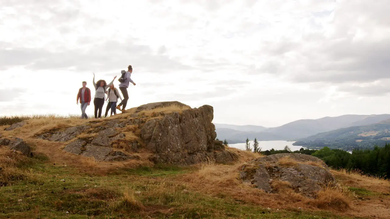 A group of five happy young adult friends arrive at the summit cheering with arms in the air and embracing during a mountain hike