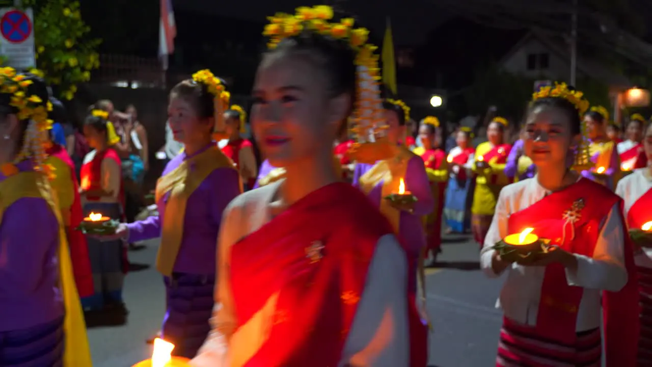 Traditional Thai women holding candles walking in front of camera smiling