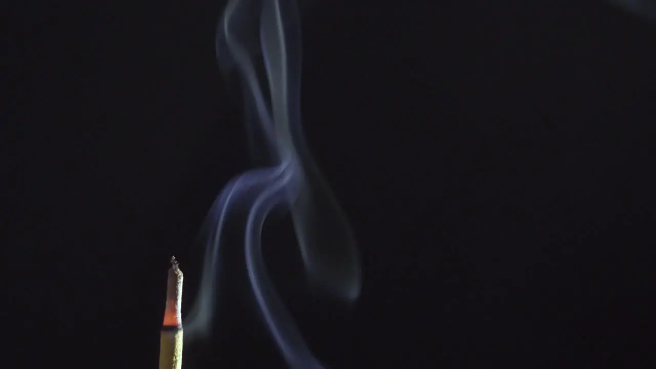 Burning incense stick smoking on simple dark black background macro copy space