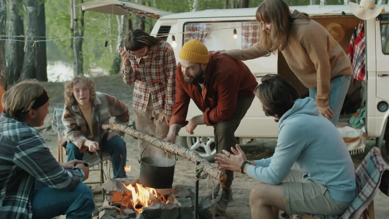 Company of Young Friends Cooking Food and Chatting by Campfire