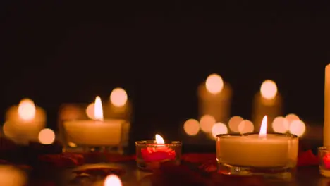 Eye Level Shot Of Romantic Lit Candles On Black Background Covered In Rose Petals With Copy Space 1