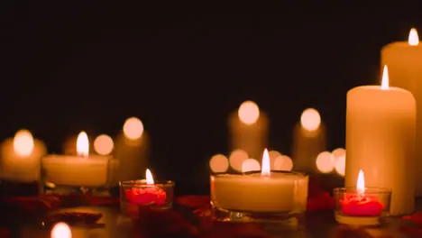 Eye Level Shot Of Romantic Lit Candles On Black Background Covered In Rose Petals With Copy Space