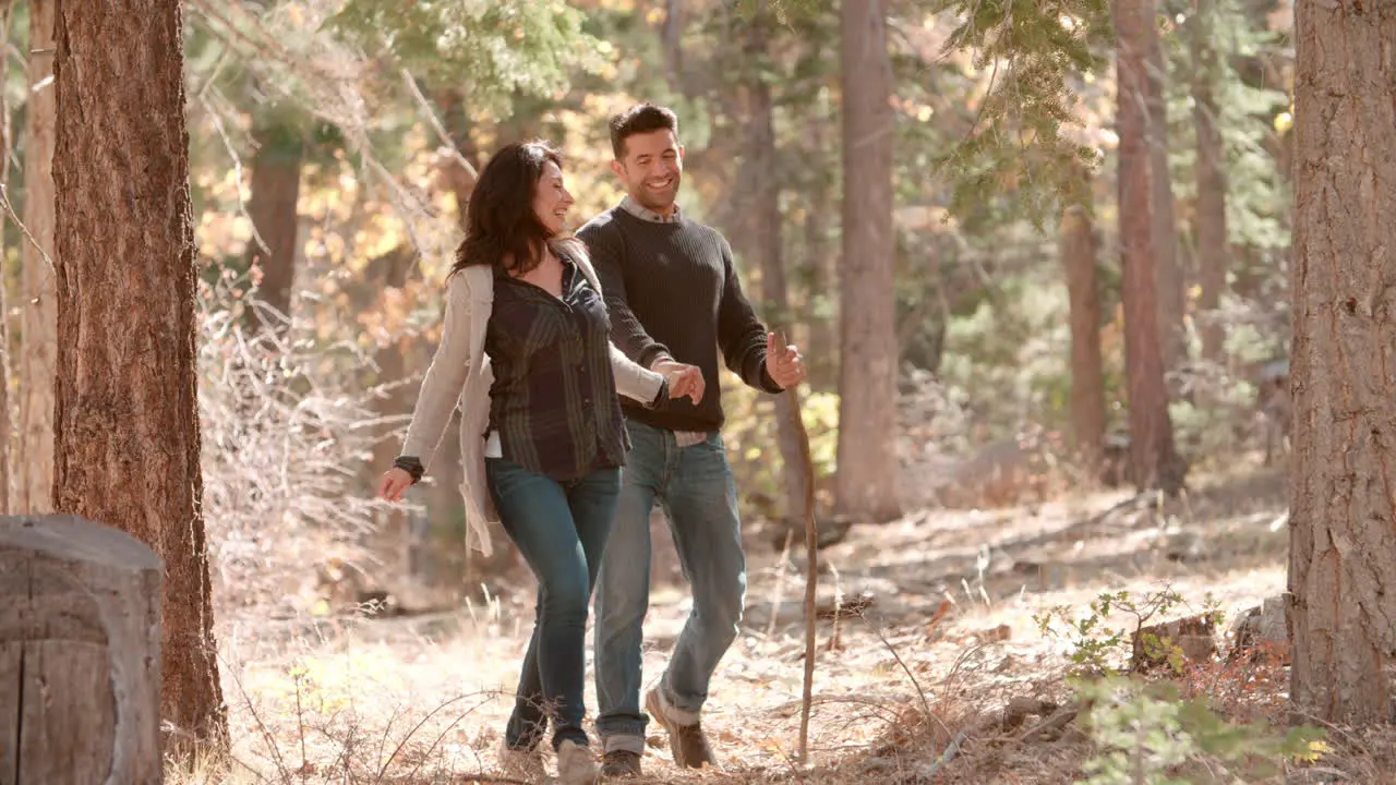 Happy Hispanic couple hold hands walking together in forest