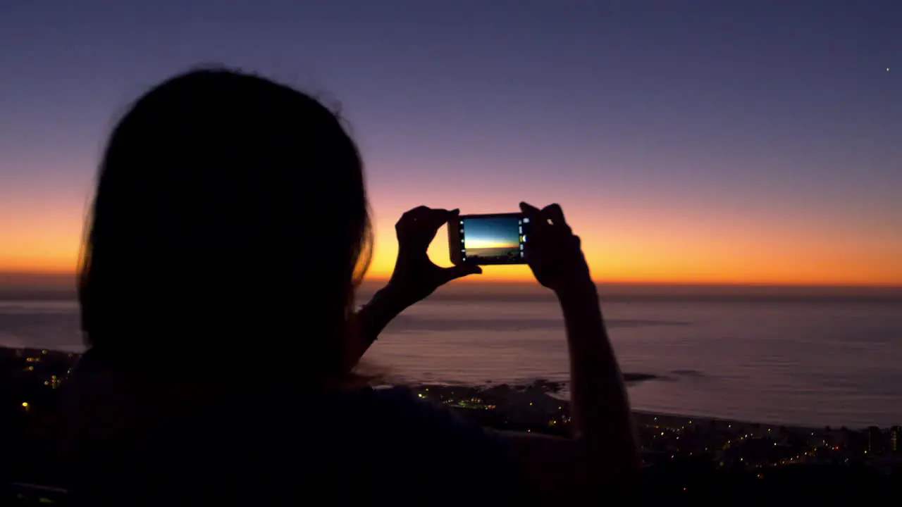 Woman taking photos with phone on beach silhouette at sunset